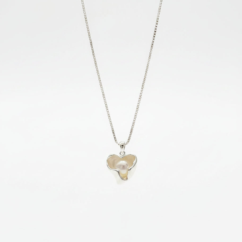 Silver necklace with a heart-shaped pendant held in a hand against a blurred background