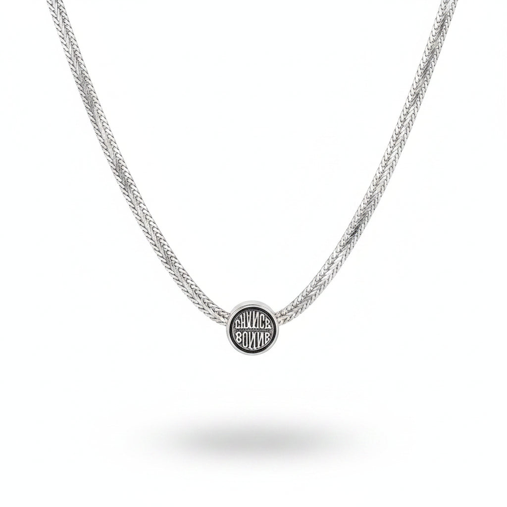 Silver necklace with a round pendant on a person wearing a white garment.
