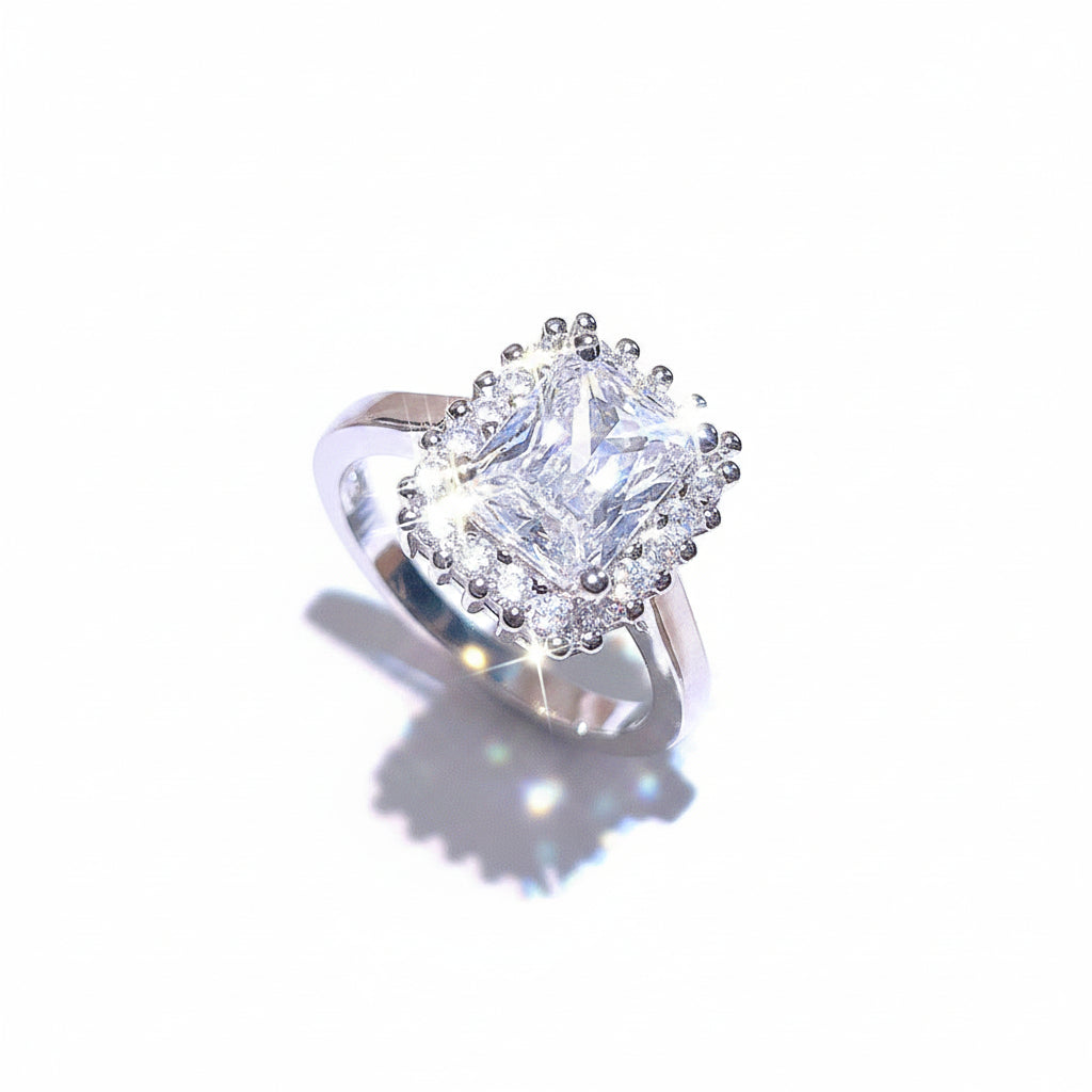 Silver ring with a large diamond and smaller diamonds on a light pink background