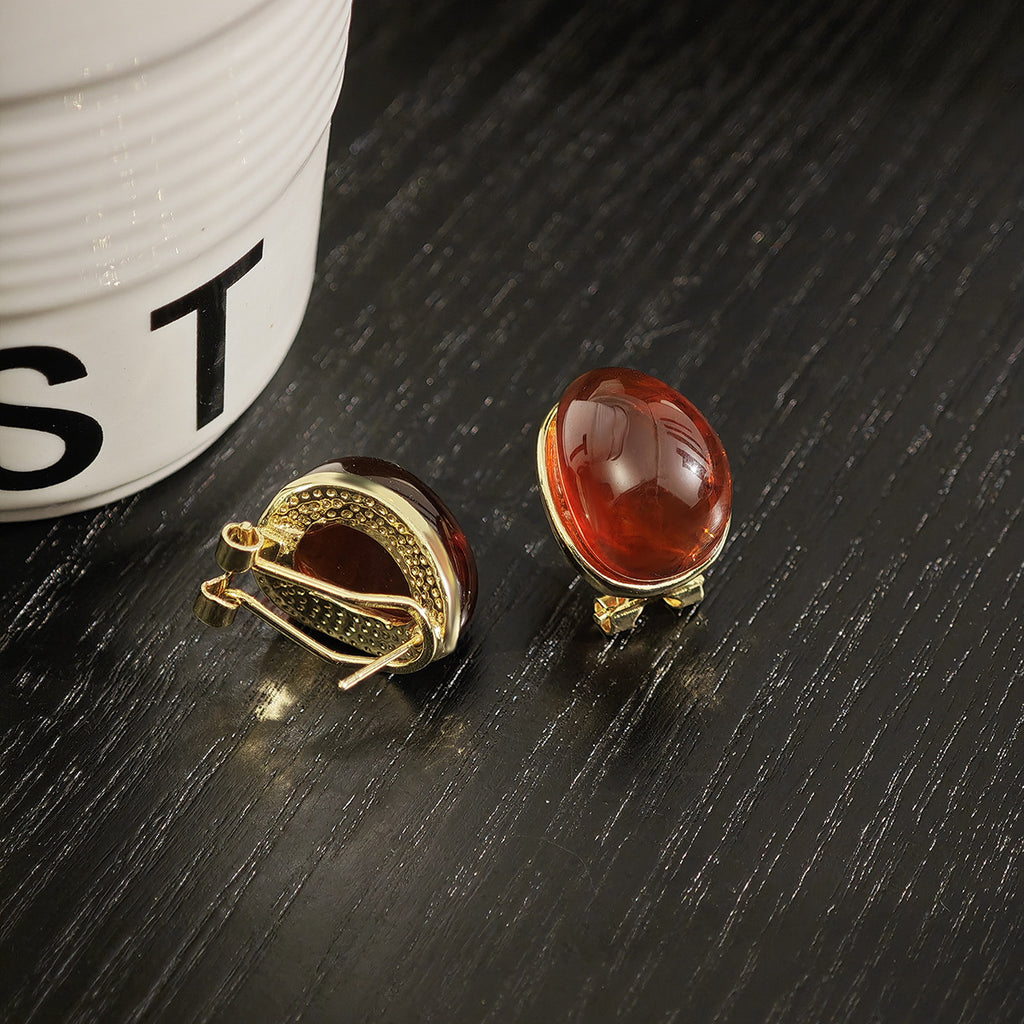 Two amber-colored gemstone earrings on a dark surface with a white container in the background.
