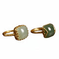 Two gold-rimmed jade rings on a wooden surface with blurred red berries in the background.