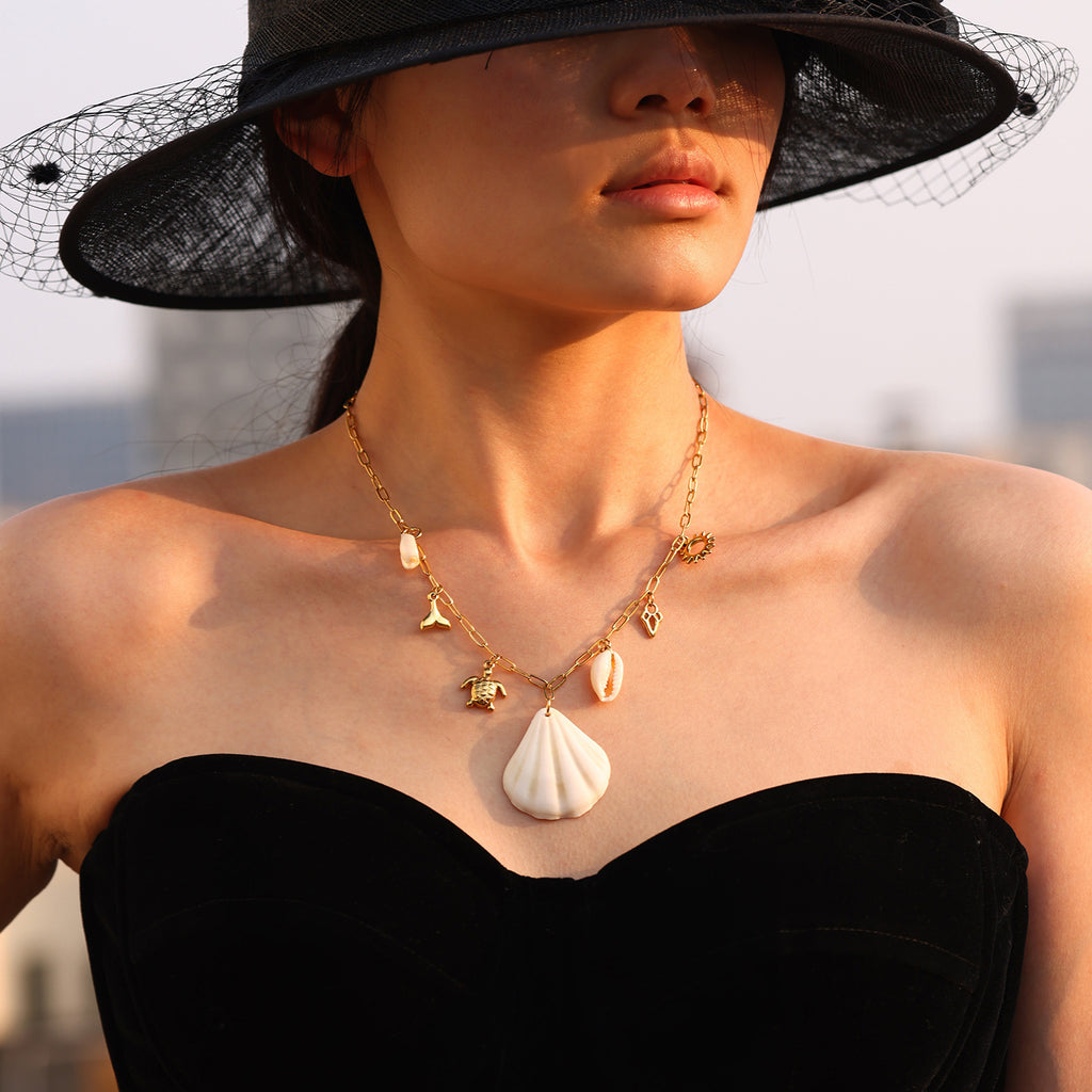 Woman wearing a black hat and black dress with a gold necklace featuring a shell pendant.