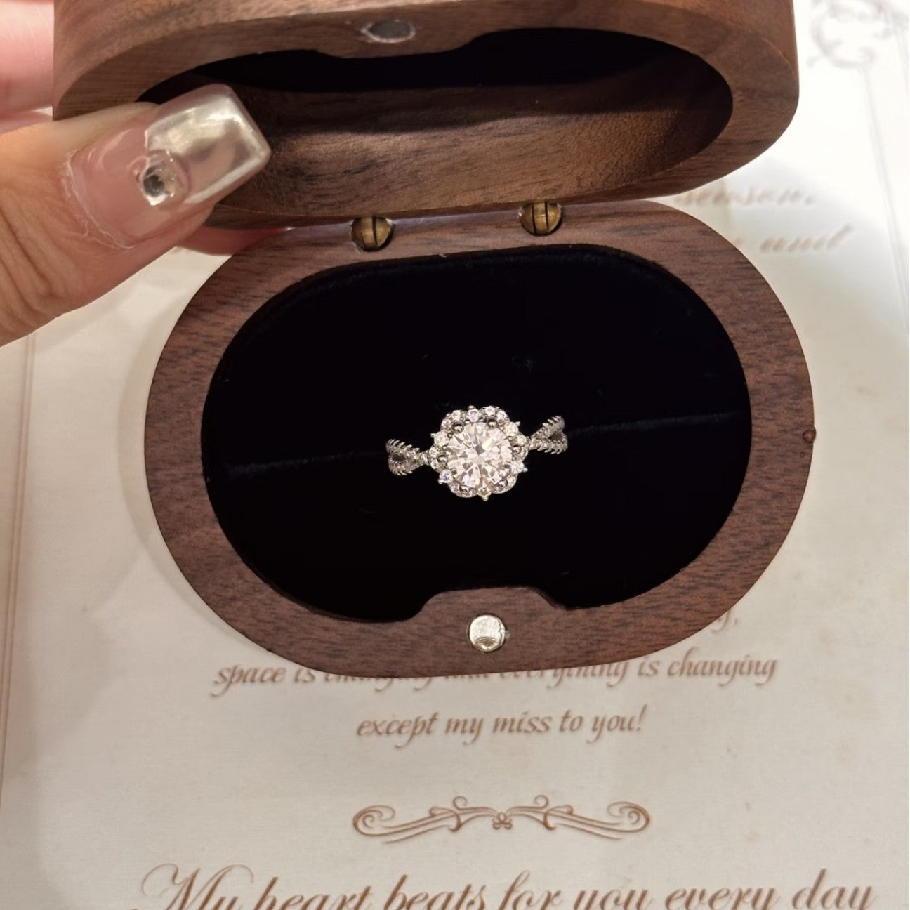 Wooden jewelry box with a diamond ring inside, held by a hand.
