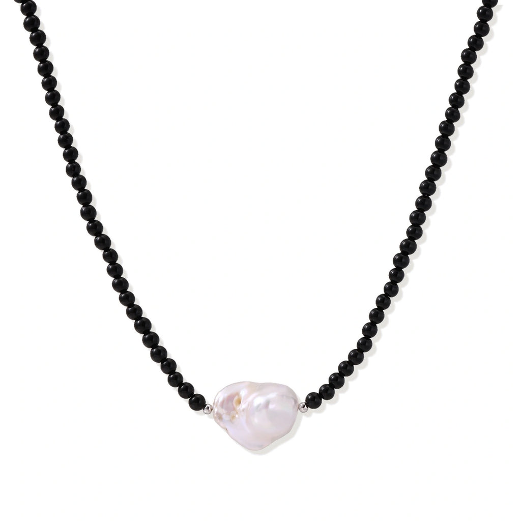 Beaded black agate necklace with iridescent baroque freshwater pearl centerpiece on cream background, front view